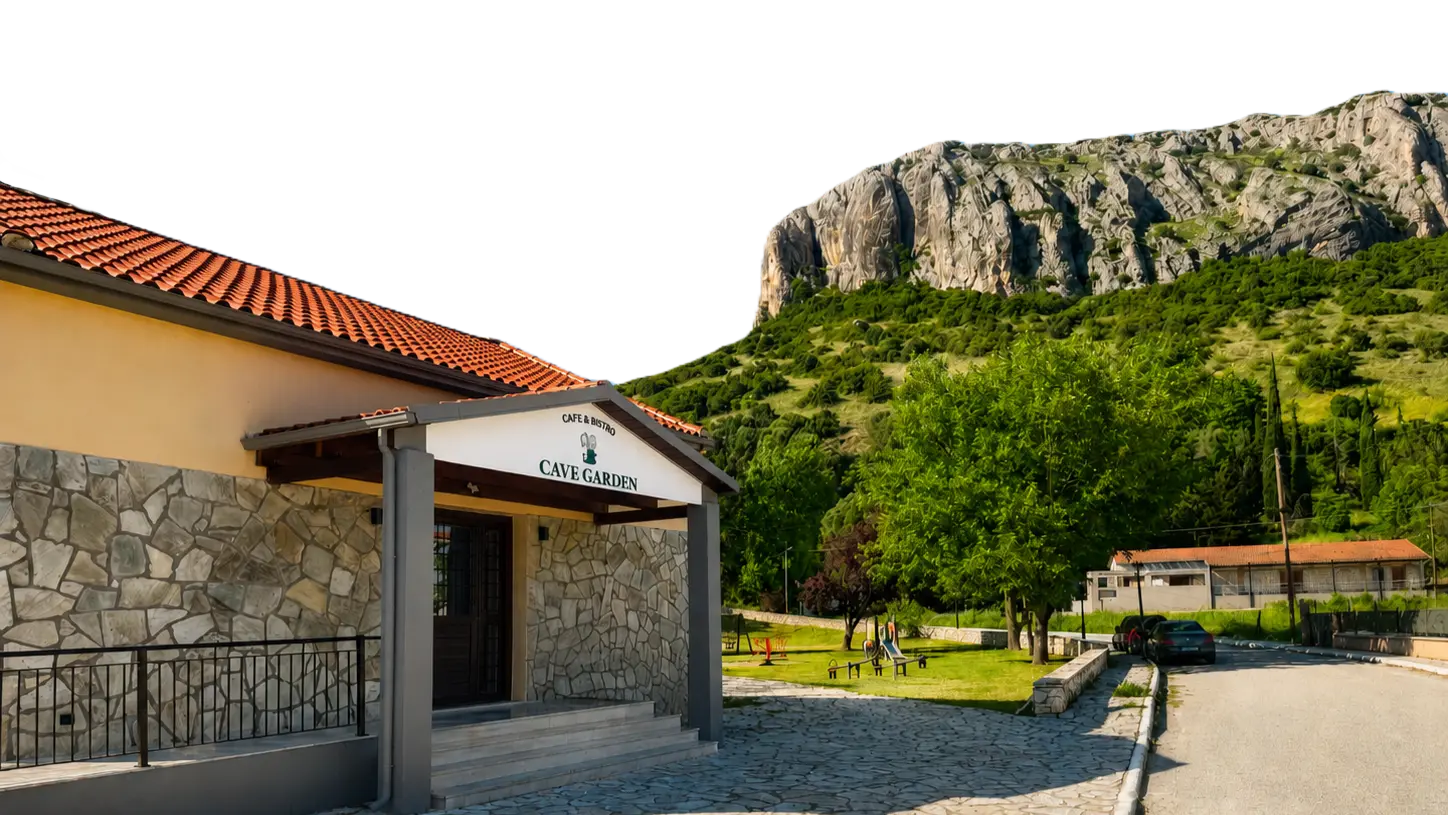 Η εξωτερική όψη του Cave Garden Cafe & Bistro με φόντο τον καταπράσινο λόφο και το βουνό